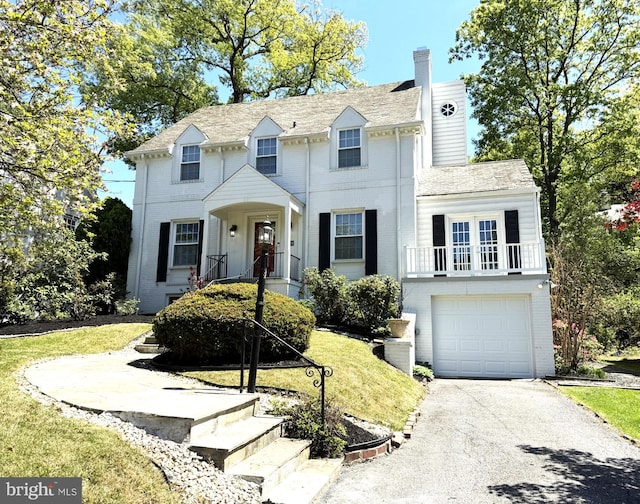 view of front of home featuring a chimney, aphalt driveway, a balcony, a front lawn, and an attached garage