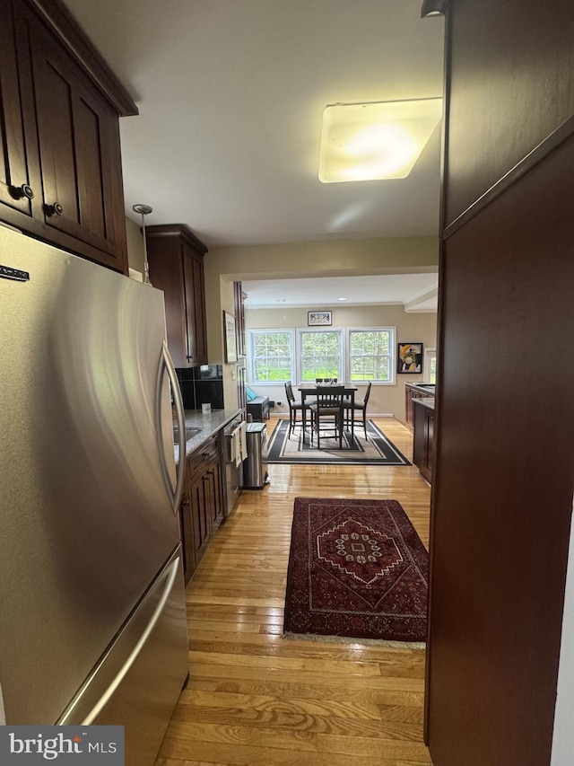 kitchen with light wood finished floors, dark brown cabinetry, freestanding refrigerator, and light stone counters