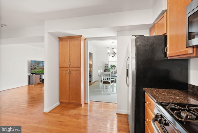 kitchen featuring a chandelier, dark stone counters, stainless steel microwave, baseboards, and light wood-type flooring