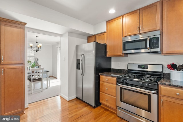 kitchen with an inviting chandelier, light wood-type flooring, recessed lighting, dark stone counters, and appliances with stainless steel finishes