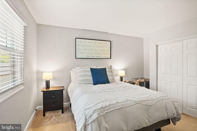 bedroom with baseboards, a closet, and light colored carpet