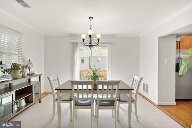 dining space featuring visible vents, crown molding, a notable chandelier, and light wood-type flooring
