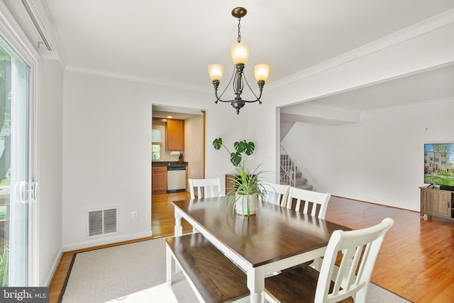 dining room featuring visible vents, light wood finished floors, a notable chandelier, ornamental molding, and stairs
