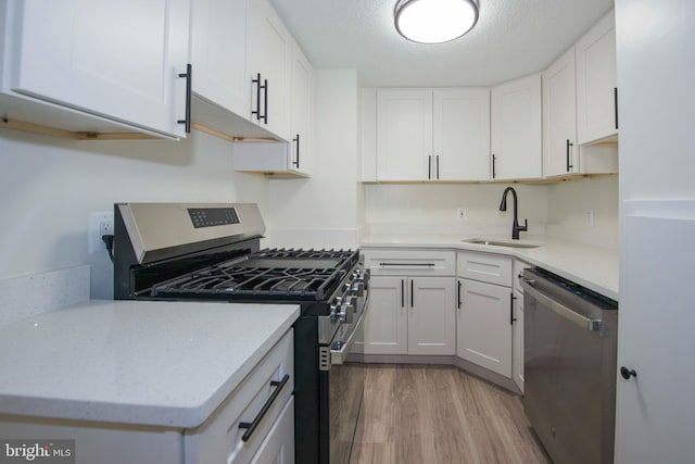 kitchen with white cabinetry, a sink, appliances with stainless steel finishes, light wood-type flooring, and light stone countertops