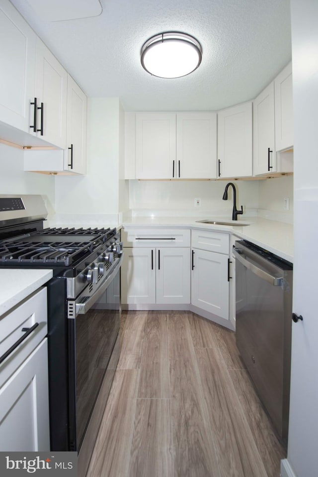 kitchen featuring white cabinets, light wood-style flooring, a sink, stainless steel appliances, and light countertops