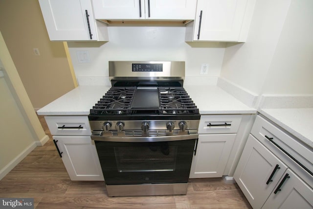 kitchen featuring baseboards, white cabinets, gas range, and wood finished floors