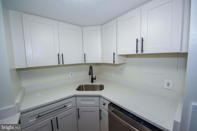 kitchen featuring a textured ceiling, stainless steel dishwasher, white cabinets, and a sink