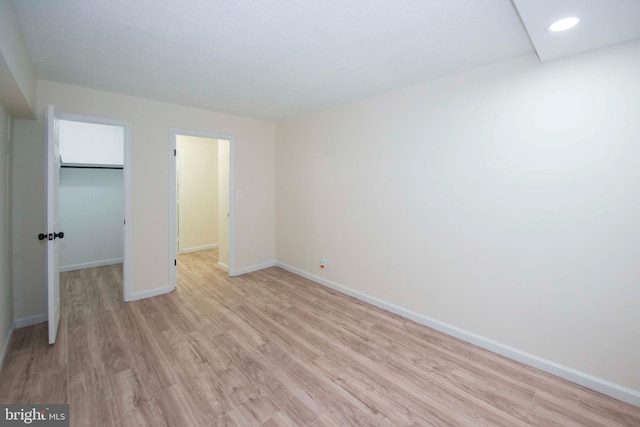 unfurnished bedroom featuring recessed lighting, light wood-style flooring, a closet, a walk in closet, and baseboards