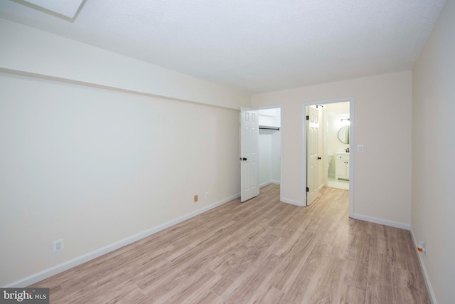 unfurnished bedroom with a closet, baseboards, light wood finished floors, ensuite bath, and a walk in closet