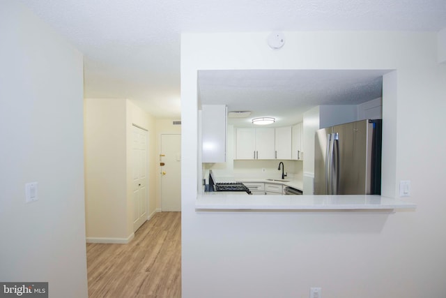 kitchen with freestanding refrigerator, light countertops, gas range oven, a sink, and light wood-type flooring