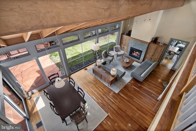 living room with a towering ceiling, a fireplace, wood finished floors, and beam ceiling