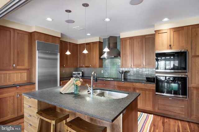 kitchen featuring a breakfast bar area, tasteful backsplash, a sink, stainless steel appliances, and wall chimney exhaust hood
