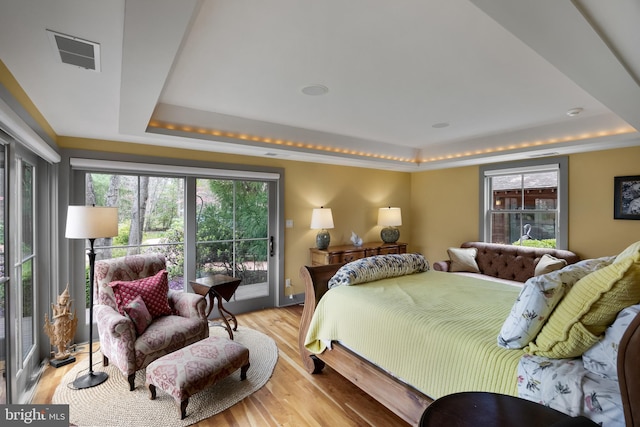 bedroom featuring access to exterior, a tray ceiling, light wood-type flooring, and visible vents