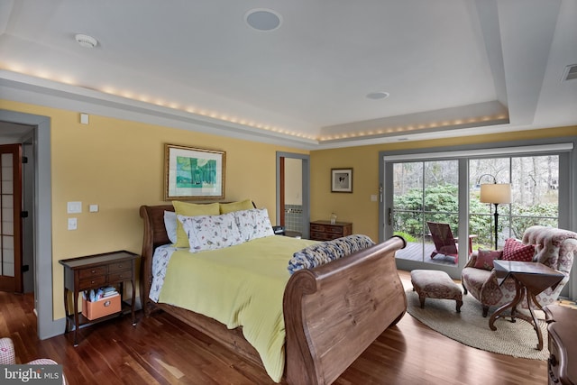 bedroom with access to outside, a raised ceiling, wood finished floors, and visible vents