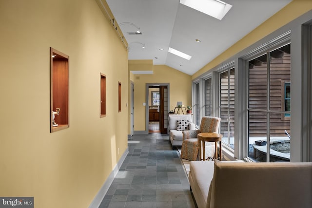 hall featuring baseboards, visible vents, and vaulted ceiling with skylight