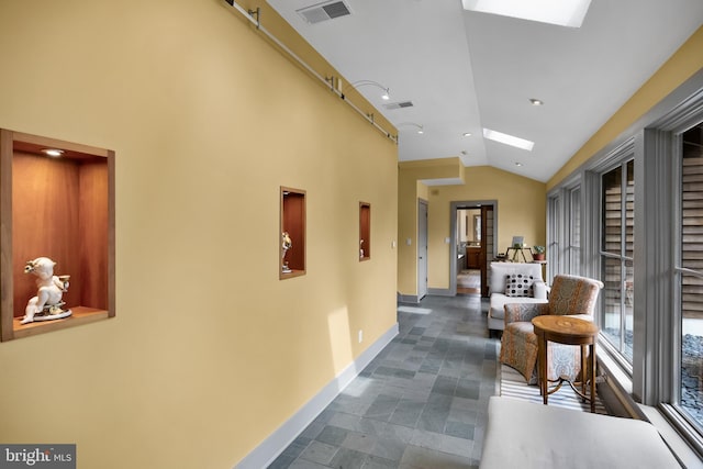 corridor with visible vents, baseboards, and vaulted ceiling with skylight