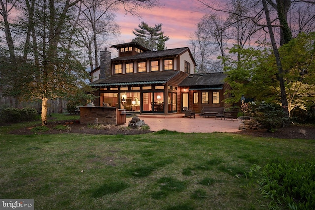 back of property at dusk with a lawn, a patio, and a chimney