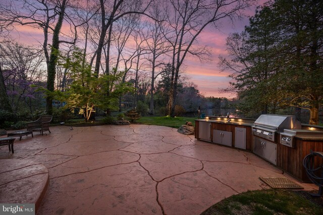 patio terrace at dusk with a sink, area for grilling, and a grill