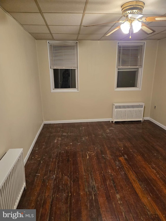 empty room featuring radiator, a paneled ceiling, visible vents, baseboards, and hardwood / wood-style floors