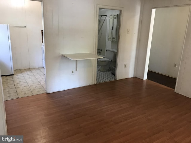 unfurnished bedroom with wood finished floors, ensuite bath, and freestanding refrigerator