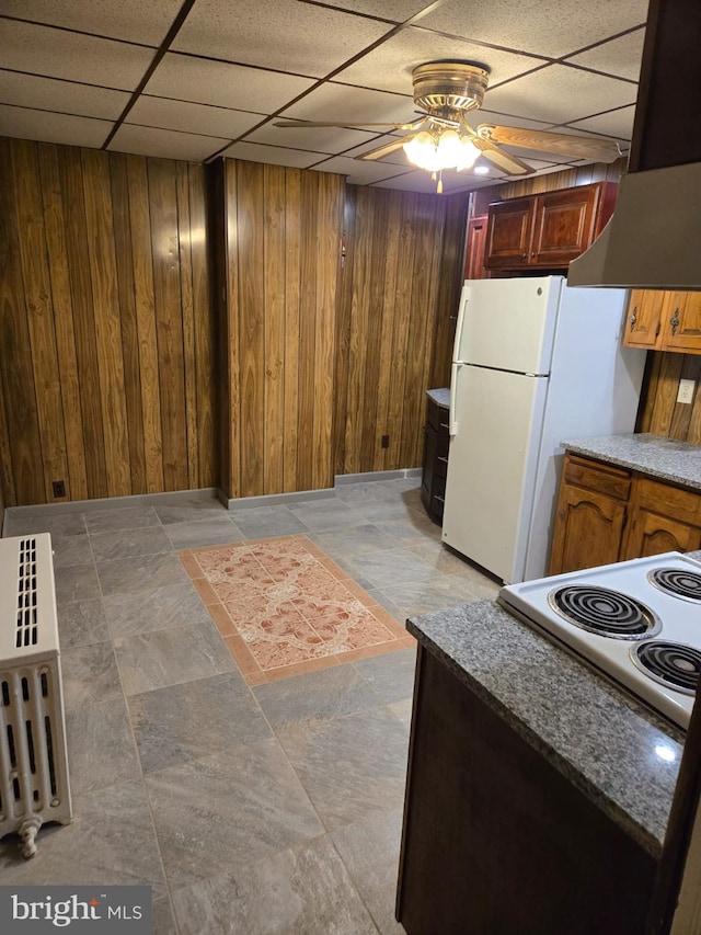 finished below grade area featuring freestanding refrigerator, a drop ceiling, stone finish floor, wood walls, and ceiling fan