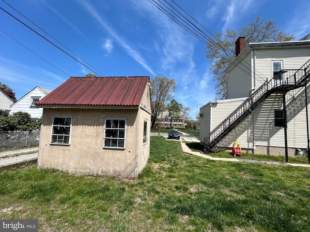 view of side of property featuring an outdoor structure, metal roof, a yard, a chimney, and fence