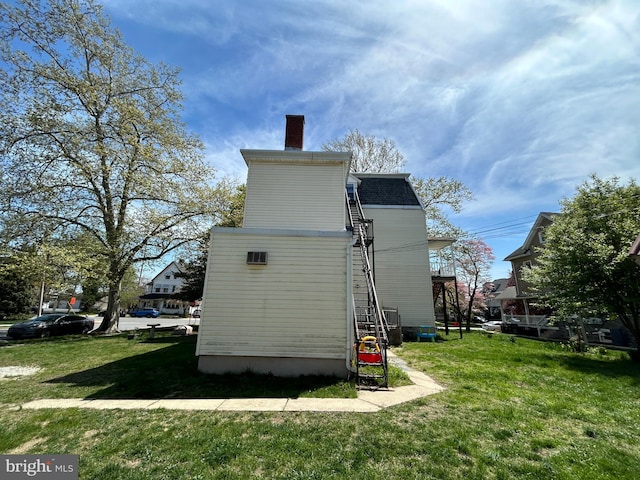 view of side of home featuring a chimney and a yard
