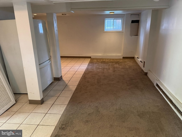 below grade area featuring light tile patterned flooring, light colored carpet, baseboard heating, freestanding refrigerator, and baseboards