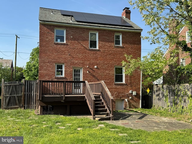 rear view of property with brick siding, a deck, and solar panels