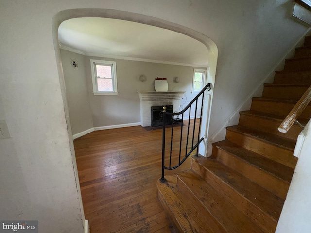 stairs with ornamental molding, arched walkways, a wealth of natural light, and hardwood / wood-style floors