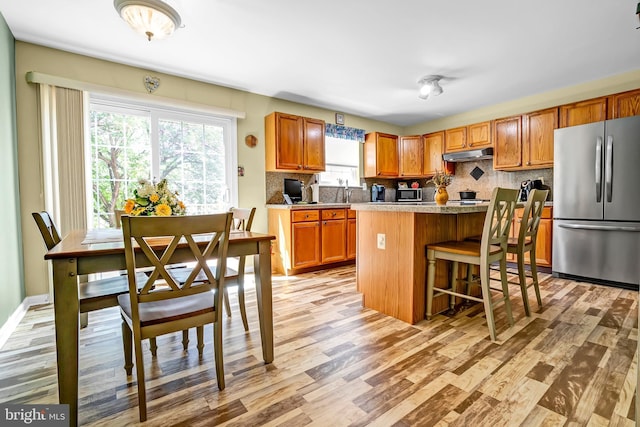 kitchen featuring stainless steel appliances, under cabinet range hood, a center island, light wood-type flooring, and tasteful backsplash
