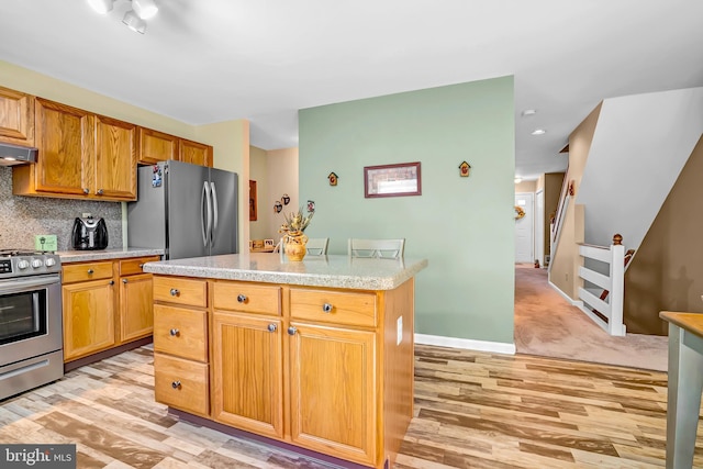 kitchen featuring appliances with stainless steel finishes, light countertops, light wood finished floors, backsplash, and a center island