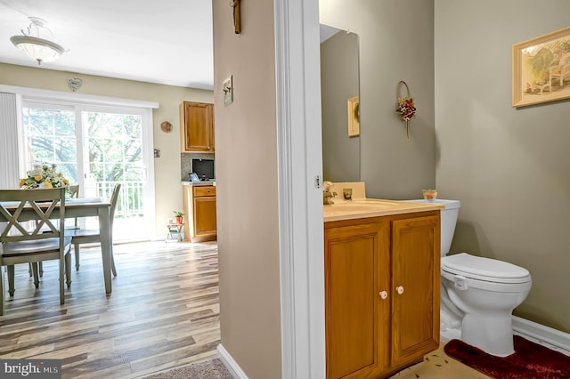 half bath with toilet, wood finished floors, baseboards, and vanity