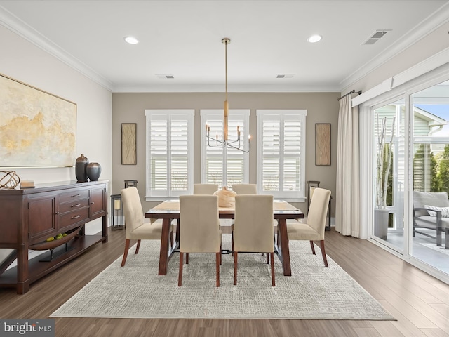 dining room with wood finished floors, ornamental molding, visible vents, and a notable chandelier