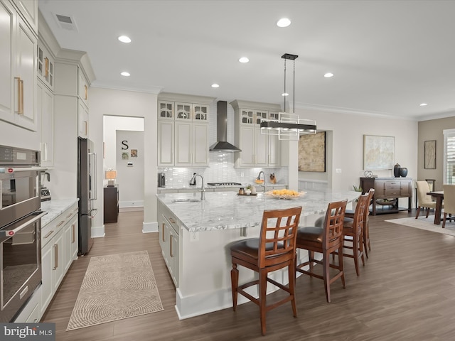 kitchen with wall chimney range hood, visible vents, appliances with stainless steel finishes, a sink, and ornamental molding