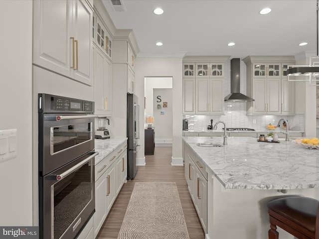 kitchen with appliances with stainless steel finishes, a sink, wall chimney exhaust hood, wood finished floors, and backsplash