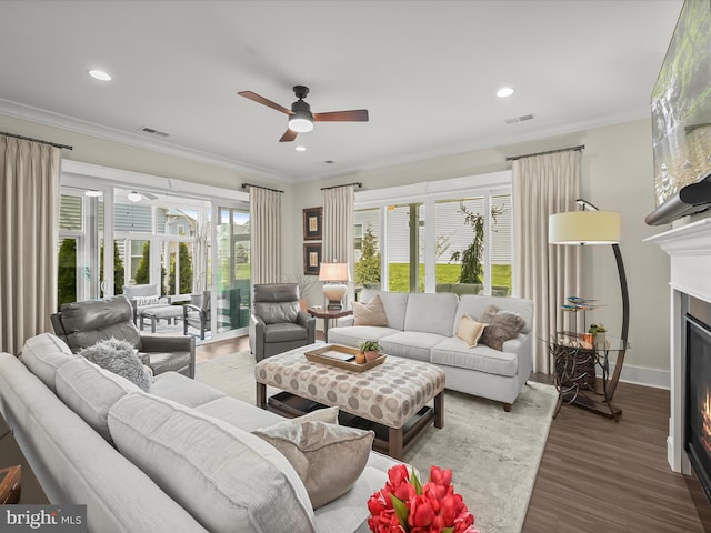living area with visible vents, a ceiling fan, wood finished floors, and a warm lit fireplace
