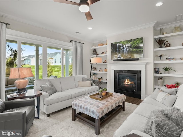 living area with crown molding, a glass covered fireplace, recessed lighting, a ceiling fan, and light wood-style flooring