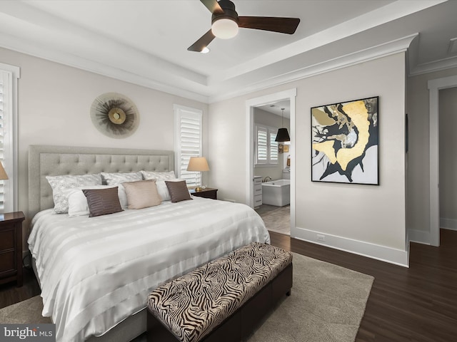 bedroom with wood finished floors, baseboards, ornamental molding, ensuite bathroom, and a tray ceiling