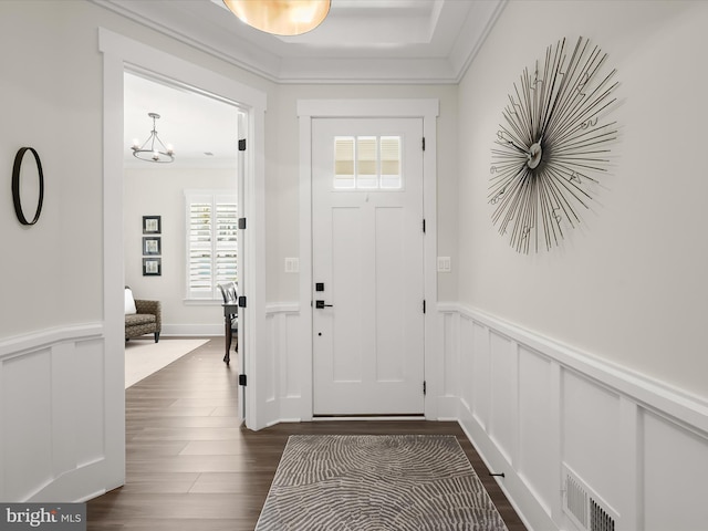 entrance foyer featuring dark wood-style flooring, visible vents, crown molding, a wainscoted wall, and a decorative wall