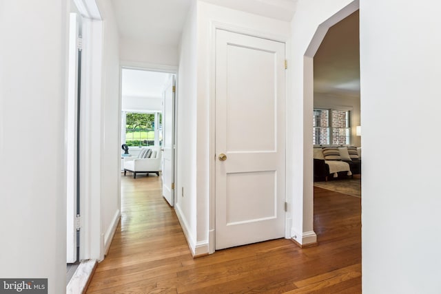 corridor with arched walkways, baseboards, and light wood-style flooring