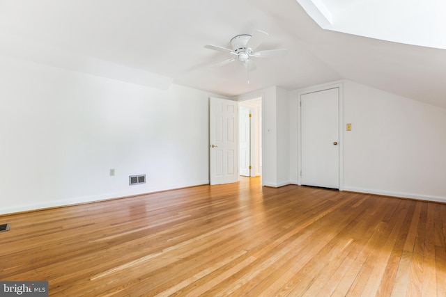 additional living space featuring a ceiling fan, visible vents, lofted ceiling with skylight, and light wood-style floors