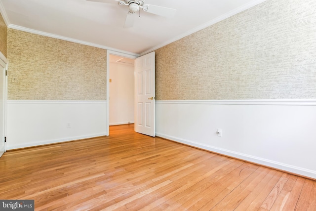 spare room featuring ceiling fan, wood finished floors, a wainscoted wall, baseboards, and ornamental molding
