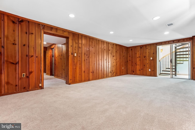 empty room with visible vents, wood walls, light carpet, stairway, and recessed lighting