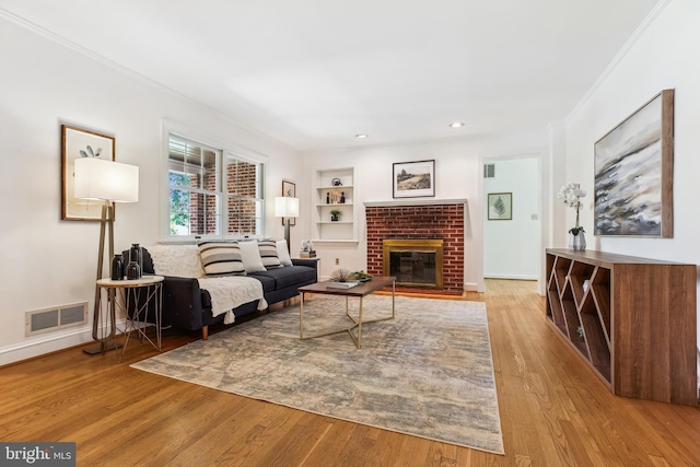 living area with visible vents, crown molding, built in features, a fireplace, and hardwood / wood-style flooring