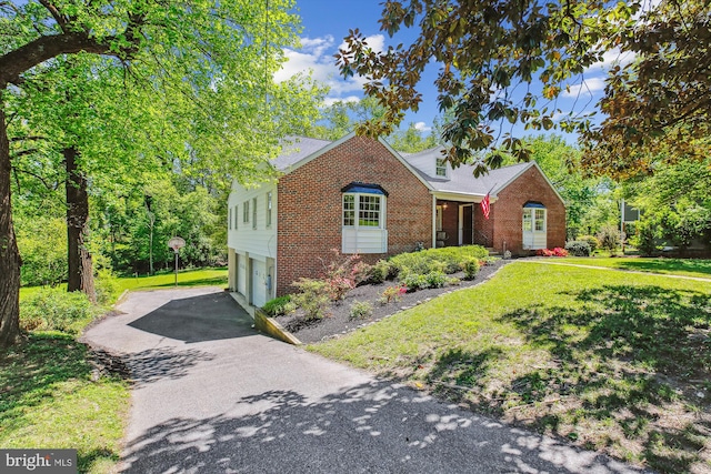 view of front of property with roof with shingles, a front yard, a garage, brick siding, and aphalt driveway