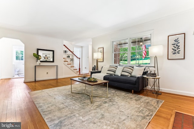 living room with arched walkways, hardwood / wood-style flooring, baseboards, and stairway