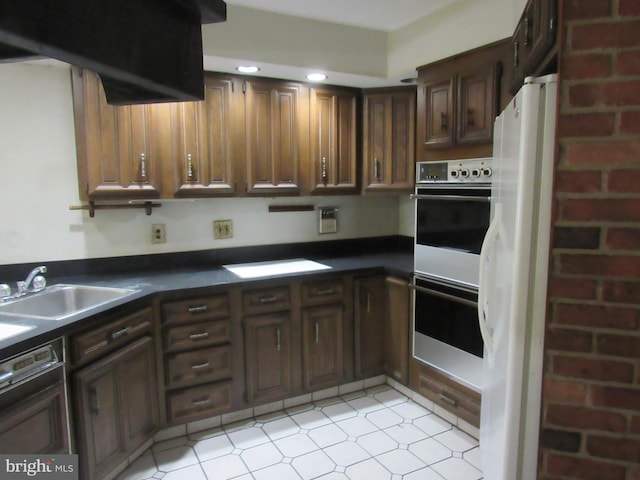 kitchen with dark countertops, dishwasher, a sink, freestanding refrigerator, and double oven