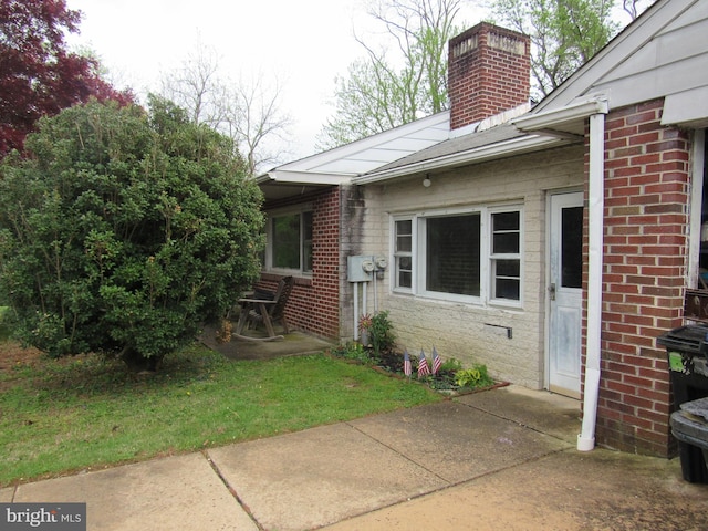 view of side of home featuring a lawn, a patio, a chimney, and brick siding