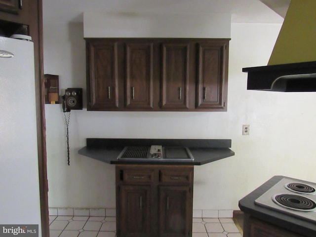 kitchen featuring wall chimney range hood, dark countertops, dark brown cabinetry, a sink, and refrigerator